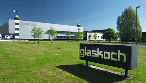 Moderner glaskoch-Firmensitz mit großer Produktionshalle, vorgelagerter Grünfläche und klar blauem Himmel