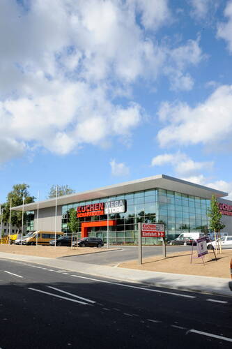 Moderner Küchen Schaffrath Megastore mit großer Glasfassade und Parkplatz an einer neu ausgebauten Straße unter blauem Himmel mit Wolken