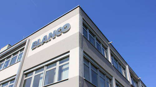 Moderne Bürohausfassade mit BLANCO-Schriftzug unter klarem, blauem Himmel
