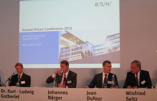 Führungskräfte von BSH diskutieren auf der Annual Press Conference 2012 in München vor einer Leinwand mit Unternehmenspräsentation