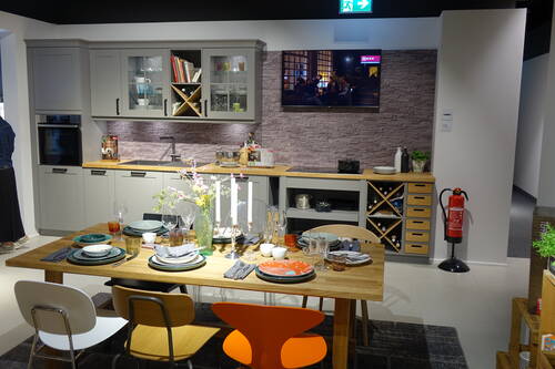 Modern eingerichtete Wohnküche mit grauen Schränken, Holzarbeitsplatte, Weinregal und Esstisch, der mit Tellern, Gläsern, Kerzen und einem Blumenstrauß für mehrere Personen gedeckt ist.