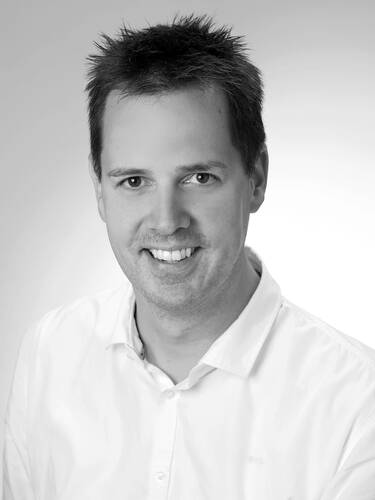 Lächelnder Mann mittleren Alters im weißen Hemd vor hellem Hintergrund in einem professionellen Schwarzweiß-Porträt