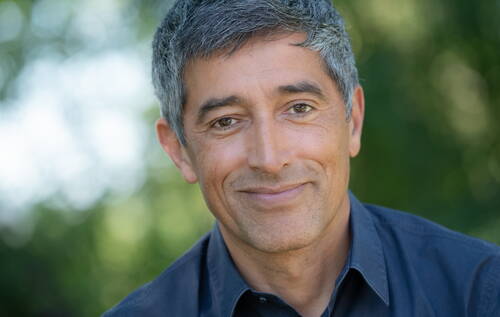 Mittelälterer Mann mit grauem Haar lächelt freundlich in die Kamera, unscharfer grüner Hintergrund im Freien