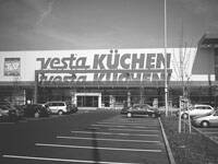 Großflächiger Vesta-Küchenmarkt mit breitem Eingangsbereich und davor liegendem, teilweise belegtem Parkplatz
