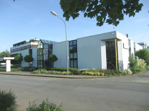 Moderner Büro- und Gewerbekomplex mit großen Glasfassaden, umgeben von gepflegten Grünanlagen an einer ruhigen Straßenecke