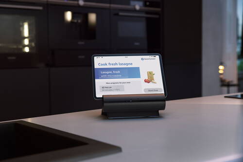 Tablet auf einer Küchenarbeitsfläche zeigt die Home-Connect-Oberfläche mit einem Programm zum frischen Lasagnebacken und der Schaltfläche „Start Oven“ vor modernen Einbauöfen im Hintergrund
