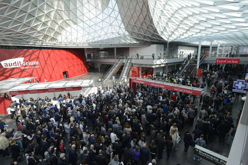 Menschenmenge drängt sich in der hellen Eingangshalle einer Messe, während Besucher an mehreren Fast-Lane-E-Ticket-Schaltern und der Rezeption anstehen und im Hintergrund Rolltreppen zum Auditorium und zu den Ausstellungshallen führen