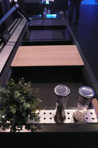 Moderne Küchenzeile mit Holzschneidebrett, integrierter Ablage mit Kräutertopf und zwei Gewürzmühlen in Edelstahloptik