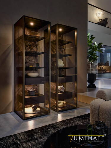 Elegantes Wohnzimmer mit zwei beleuchteten Glasvitrinen, die moderne Dekoobjekte und Gläser präsentieren, neben einem Sofa und Blick auf eine urbane Skyline im Hintergrund