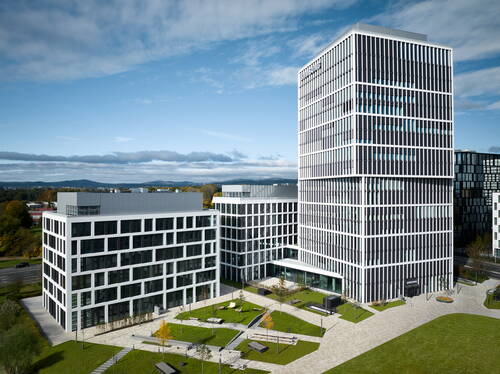 Moderner Bürokomplex mit mehreren weißen Glasfassaden-Gebäuden, zentralem begrüntem Innenhof und weitem Blick auf eine hügelige Landschaft unter blauem Himmel