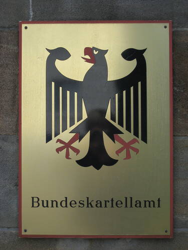 Metallschild mit Bundesadler und schwarzer Aufschrift „Bundeskartellamt“ an einer Steinwand