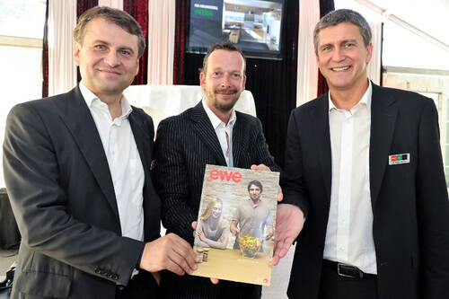 Drei geschäftlich gekleidete Männer präsentieren lächelnd ein Magazin mit dem Titel „ewe“, das sie gemeinsam in die Kamera halten.
