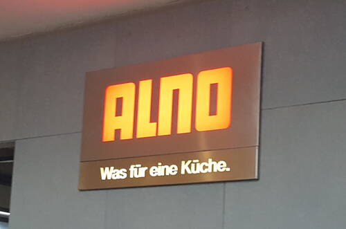 Leuchtendes ALNO-Firmenschild an einer grauen Wand mit dem Slogan „Was für eine Küche.“ in weißen Buchstaben
