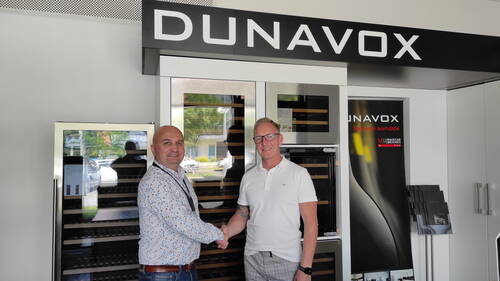 Zwei Männer schütteln sich in einem modernen Showroom der Marke Dunavox vor ausgestellten Weinkühlschränken die Hand.