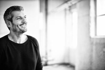Lächelnder Mann mit Bart blickt seitlich aus dem Fenster in einem hellen, unscharfen Innenraum in Schwarz-Weißaufnahme