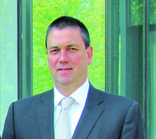 Mittelalterlicher Mann im grauen Anzug mit Krawatte steht vor Glasfassade mit grünem Hintergrund