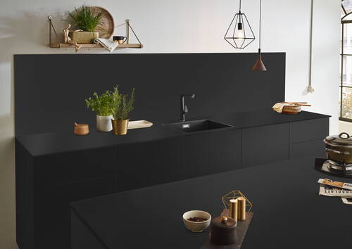 Modern gestaltete schwarze Küchenzeile mit eingelassenem Spülbecken, frischen Kräutertöpfen, schwebendem Wandregal und minimalistischer Pendelleuchte im skandinavischen Stil.
