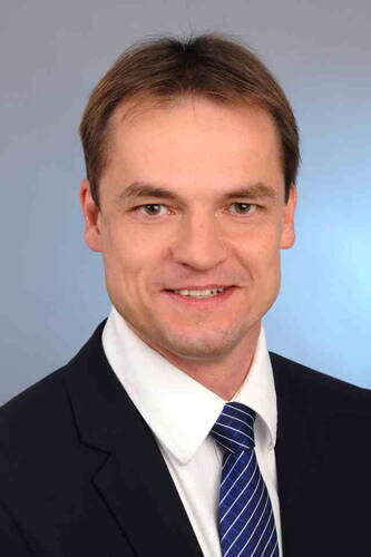 Lächelnder Mann im Anzug mit blau-gestreifter Krawatte vor neutral graublauem Hintergrund
