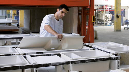 Mitarbeiter in einer Fabrik überprüft sorgfältig eine weiße Sanitärkeramik in einer Reihe frisch gegossener Waschbeckenformen