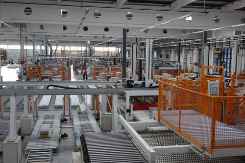 Modern automatisierte Produktionshalle mit Förderbändern, Robotern und wenigen Mitarbeitenden zwischen hohen Maschinenreihen