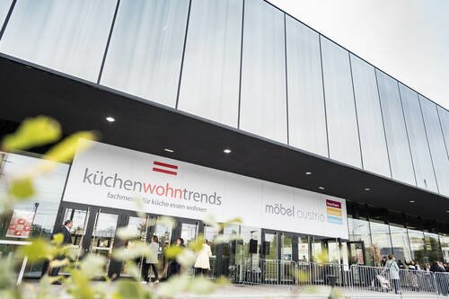 Besucher betreten den verglasten Messe-Eingang zur „küchenwohntrends“ und „möbel austria“, dessen moderne Fassade sich über die gesamte Bildbreite erstreckt.