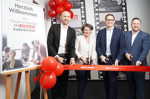 Vier Geschäftsleute durchschneiden gemeinsam ein rotes Band zur feierlichen Eröffnung des Akademie-Standorts XXXLutz dodenhof in Kaltenkirchen, umrahmt von roten Luftballons und einem Begrüßungsplakat.