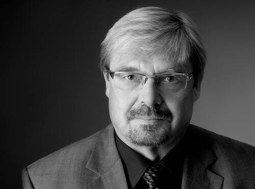 Älterer Mann mit Brille, Schnurrbart und kurzem hellen Haar im Anzug, der in einem schwarz-weißen Porträt ernst in die Kamera blickt.
