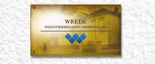 Messingschild an einer hellen Putzfassade mit der Aufschrift „WREDE Industrieholding GmbH & Co. KG“ und blauem Rautensymbol darunter