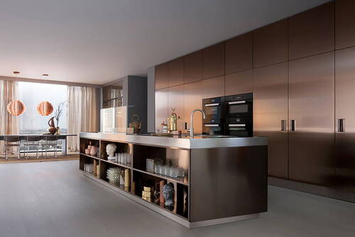 Elegante Designküche mit bronzefarbenen Hochglanzfronten, großer Kochinsel aus Metall und Glasregalen, die zu einem Essbereich mit bodentiefen Fenstern und modernen Pendelleuchten übergehen