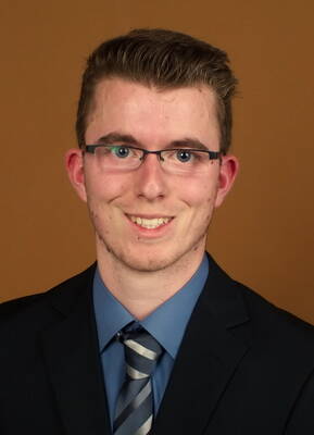 Junger Mann mit Brille und Anzug lächelt vor einfarbig braunem Hintergrund in einem formellen Porträt