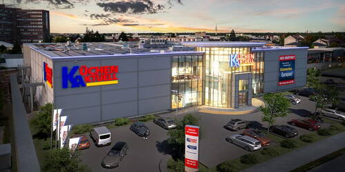 Modernes Küchenstudio-Gebäude von Küchen Aktuell in der Abenddämmerung mit beleuchteter Glasfassade und voller Parkplatzfläche davor