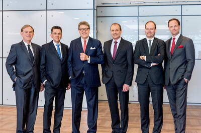 Sechs Geschäftsleute in Anzügen stehen nebeneinander in einem modernen Konferenzraum und lächeln in die Kamera