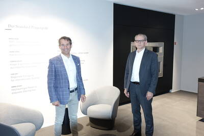 Zwei Geschäftsleute stehen in einem modernen Showroom von Poggenpohl vor einer Wand mit Markenbotschaften und einer schwarzen Einbauküche im Hintergrund