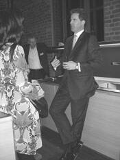 Elegant gekleideter Mann im Anzug unterhält sich locker mit einer Frau in gemustertem Kleid in einer Bar vor Backsteinwand