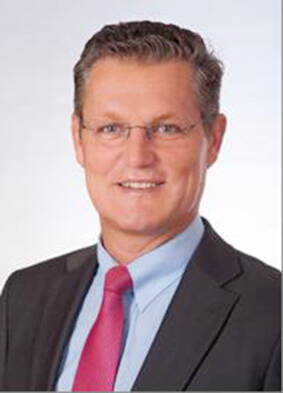 Mittelälterlicher Mann im Anzug mit rosa Krawatte und Brille lächelt freundlich vor neutralem Hintergrund