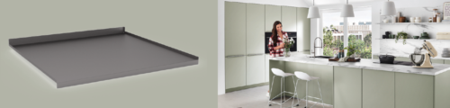 Dunkelgraue, flache Metall-Tablettauflage neben einer modernen, hellen Wohnküche mit mintgrünen Fronten und Kochinsel, an der eine Frau kocht.