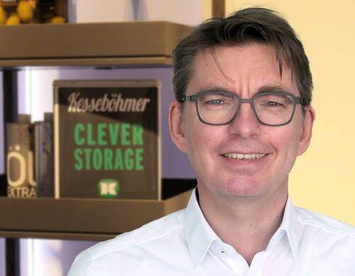 Mittelälterer Mann mit Brille und weißem Hemd lächelt in die Kamera, im Hintergrund ein Regal mit der Aufschrift „Kesseböhmer Clever Storage“.