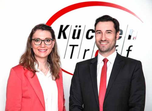 Zwei lächelnde Geschäftsleute im Anzug vor einem KüchenTreff-Logo auf weißem Hintergrund