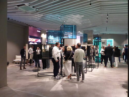 Messebesucher unterhalten sich in einer modernen Ausstellungshalle mit beleuchteten Präsentationsinseln und Küchen-Geräten von Siemens.