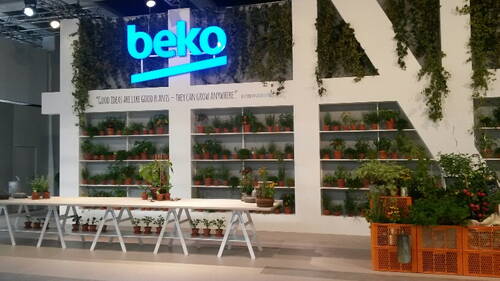 Messestand von Beko mit beleuchtetem Firmenlogo, begrünten Wänden und zahlreichen Topfpflanzen auf Regalen und langen Holztischen