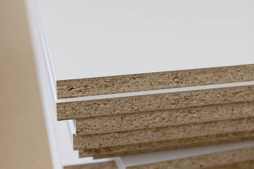 Mehrere übereinander gestapelte, weiß beschichtete Spanplatten zeigen ihre grobe Holzstruktur an den Schnittkanten