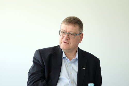 Mittelalterlicher Mann im dunklen Anzug und mit Brille sitzt vor hellem Hintergrund und blickt nachdenklich zur Seite