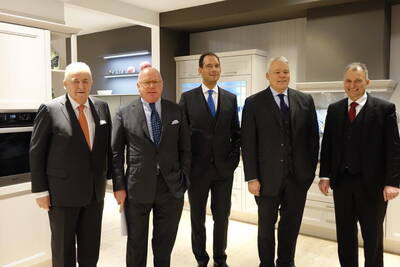 Fünf elegant gekleidete Männer im Anzug stehen lächelnd nebeneinander in einer modernen Ausstellungsküche.