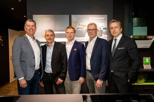 Fünf Männer in Anzügen stehen lächelnd nebeneinander in einer modernen Küchenausstellung vor beleuchteten Werbetafeln der Marken berbel und Beckermann Küchen.