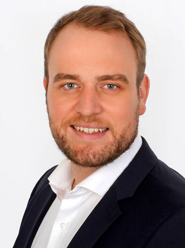 Junger Mann im Anzug mit weißem Hemd lächelt freundlich in einem professionellen Porträt vor weißem Hintergrund