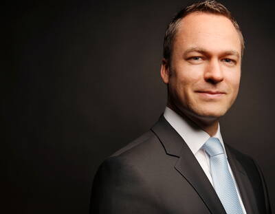 Selbstbewusst lächelnder Geschäftsmann im dunklen Anzug mit hellblauer Krawatte vor dunklem, neutralem Hintergrund