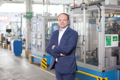 Geschäftsmann im Anzug steht mit verschränkten Armen selbstbewusst in einer modernen Industriehalle vor Maschinenanlagen