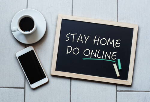Kaffeetasse, Smartphone und Tafel mit der Aufschrift „Stay home do online“ liegen auf hellen Fliesen nebeneinander