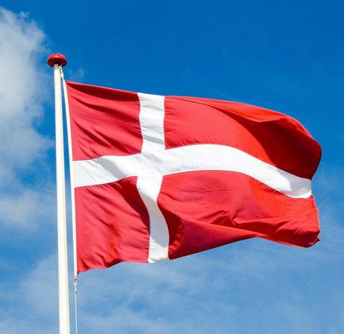 Rote Flagge mit weißem Kreuz weht an einem Fahnenmast vor blauem Himmel mit wenigen Wolken