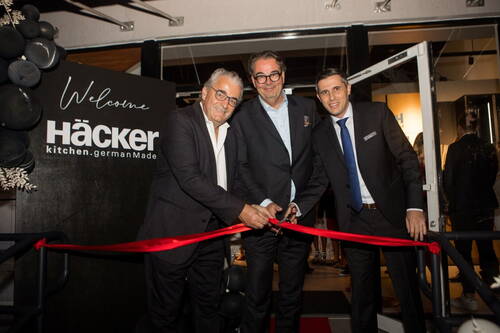 Drei elegant gekleidete Männer schneiden ein rotes Band zur feierlichen Eröffnung eines Häcker Küchenstudios am Eingang des Showrooms durch.